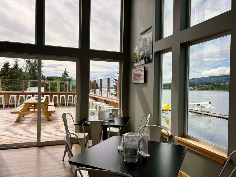 Cafe with large windows overlooking a lake and mountain scenery.