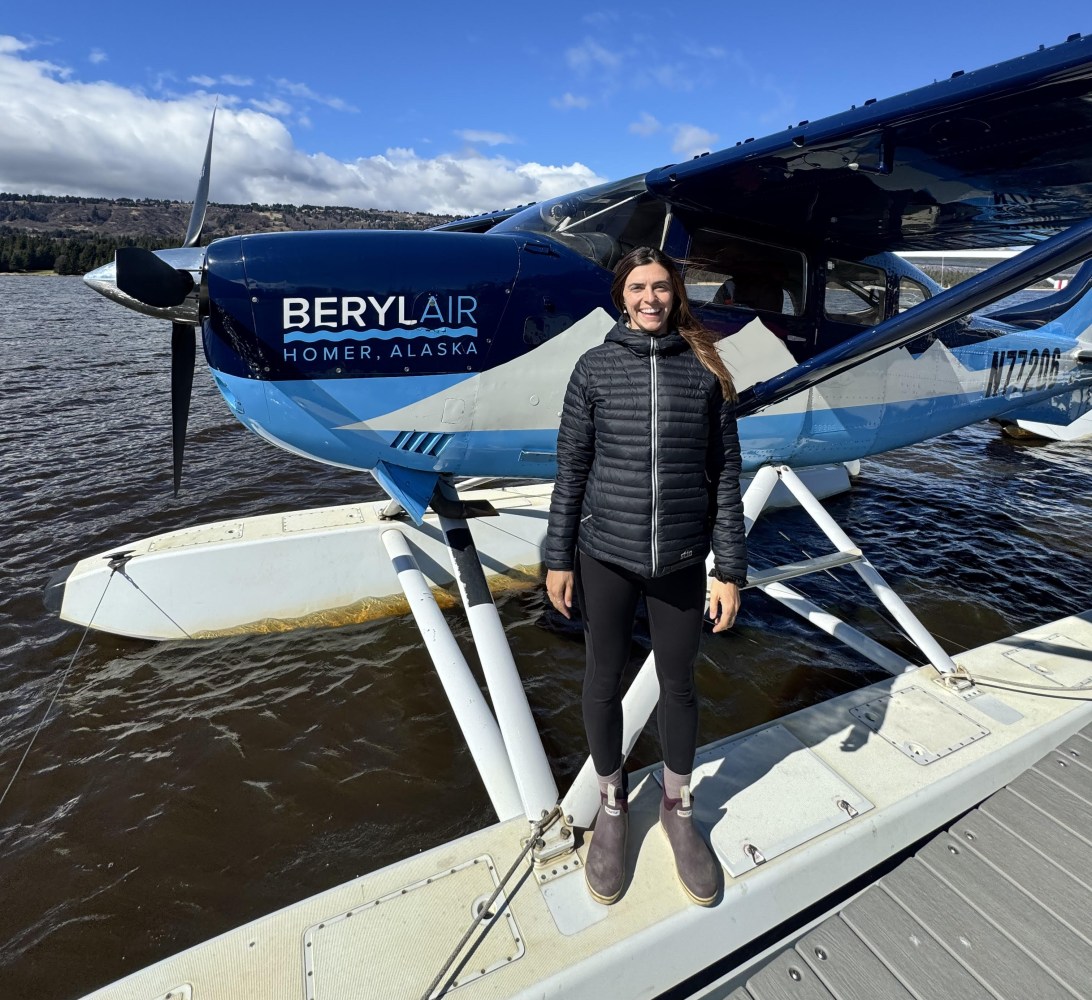 Person standing on dock next to a blue and white seaplane.